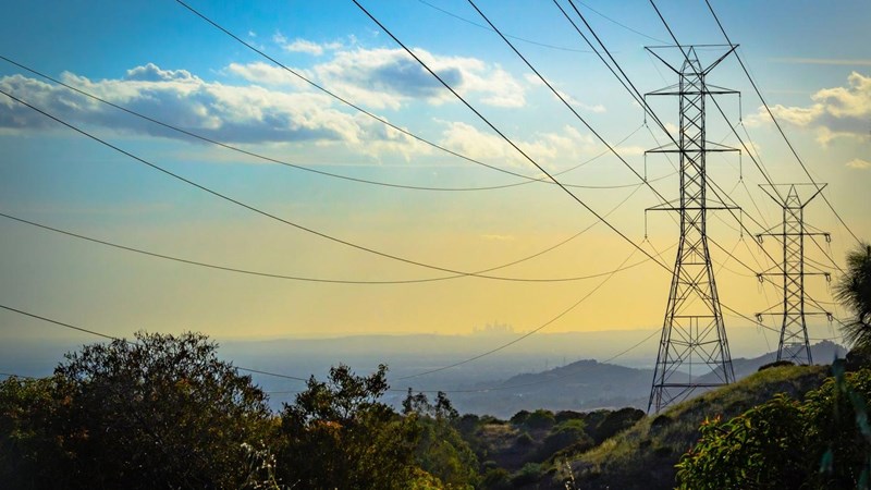 High voltage pylons on a hillside and a city visible in the distant background.