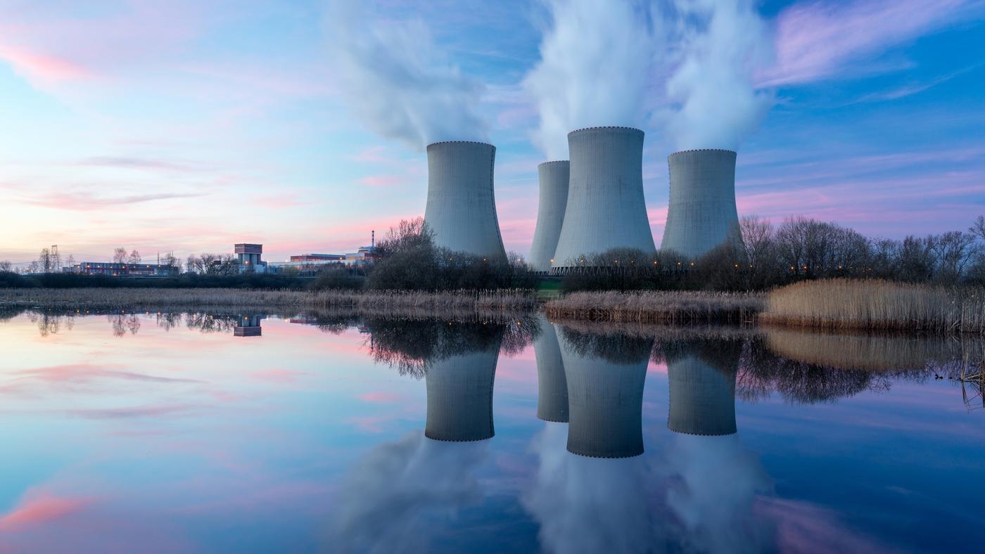 Four operational nuclear cooling towers reflecting in a lake at sunset.