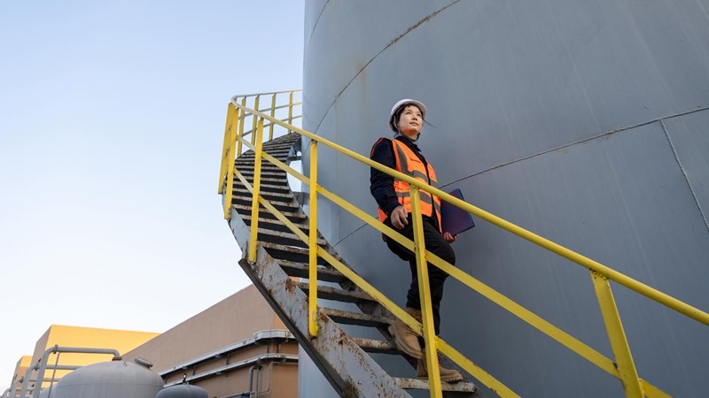 A female engineer walking dow the exterior steps of a fuel tank, at a chemical plant.