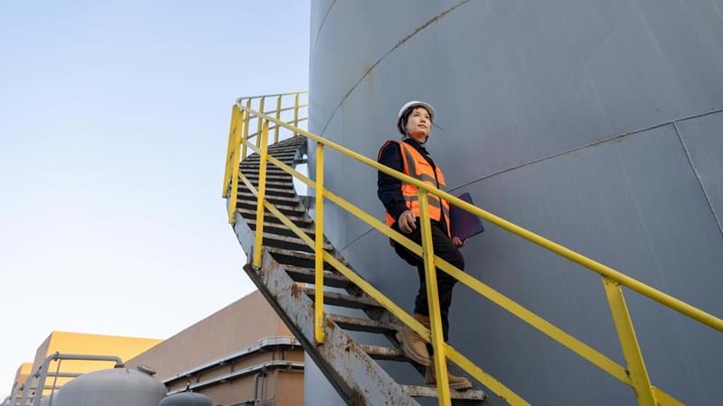A female engineer walking dow the exterior steps of a fuel tank, at a chemical plant.