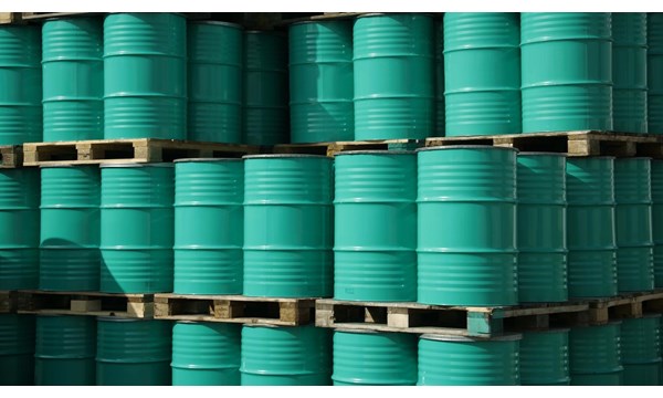 Pile of green industrial barrels stored outside a warehouse.