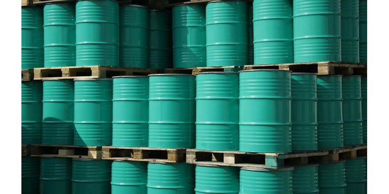 Pile of green industrial barrels stored outside a warehouse.