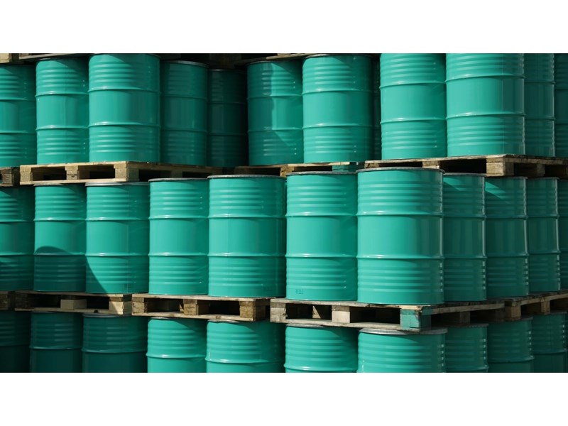 Pile of green industrial barrels stored outside a warehouse.