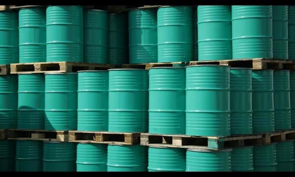 Pile of green industrial barrels stored outside a warehouse.