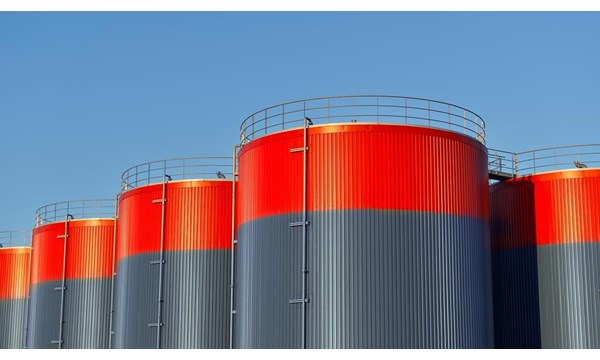 Multiple rows of connected red and grey storage tanks, with a blue sky with copy space in the background.