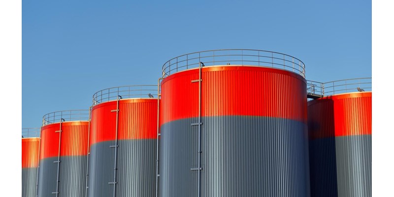 Multiple rows of connected red and grey storage tanks, with a blue sky with copy space in the background.