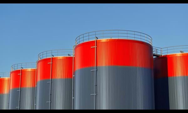Multiple rows of connected red and grey storage tanks, with a blue sky with copy space in the background.