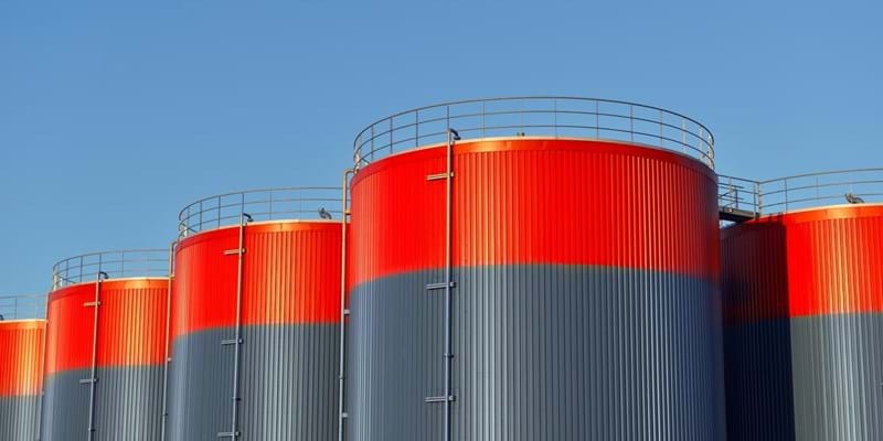 Multiple rows of connected red and grey storage tanks, with a blue sky with copy space in the background.