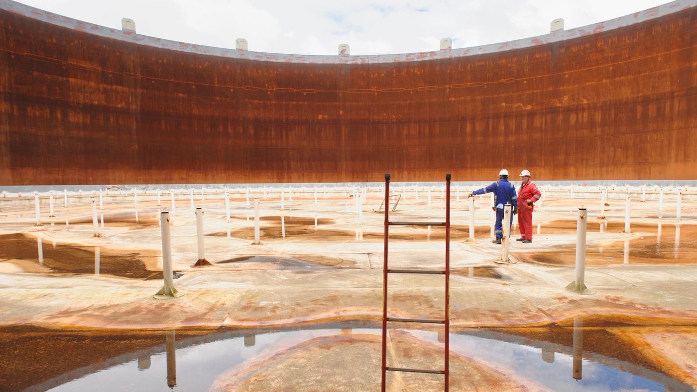 Technicians examining the interior of an empty fuel storage tank.