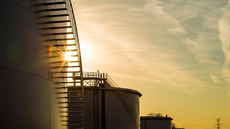 The sun is setting behind a row of oil tanks.
