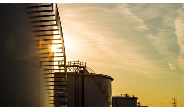 The sun is setting behind a row of oil tanks.