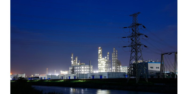 Chemical plant illuminated in the evening, next to a row of electricity pylons.