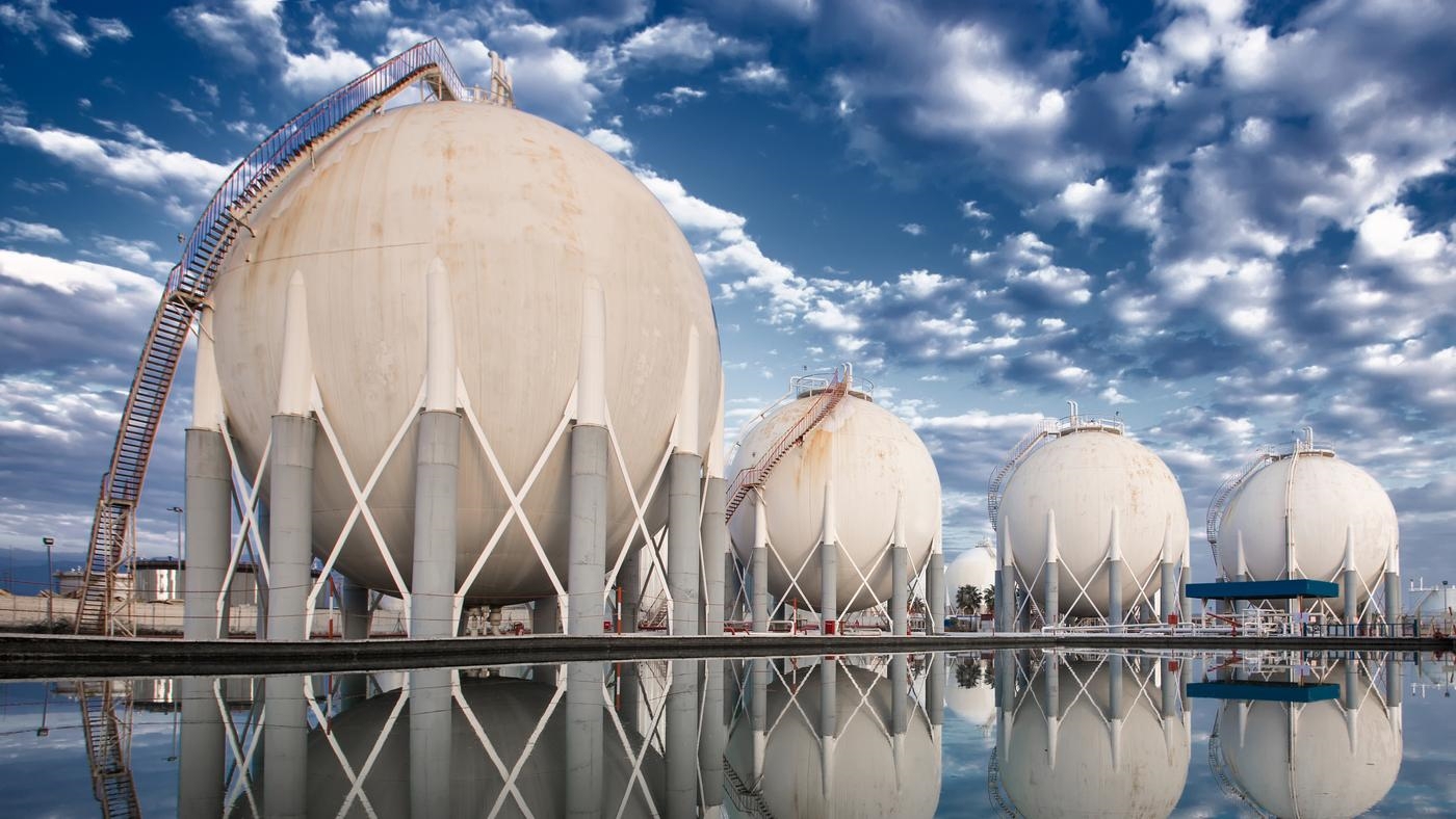 Four LNG storage tanks, reflecting in the body of water they stand at.