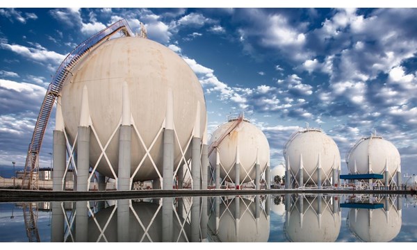 Four LNG storage tanks, reflecting in the body of water they stand at.