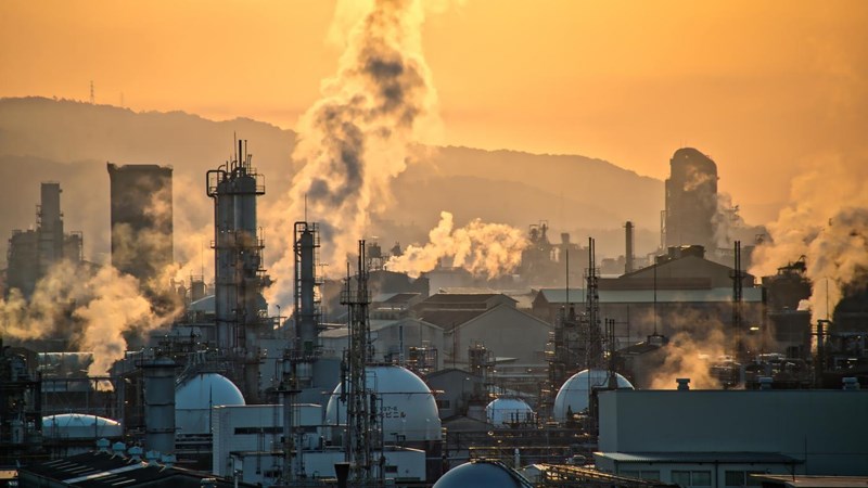 Smoke and emissions coming from a refinery, during an orange sunset.
