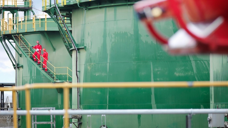 Two engineers standing on the exterior stairwell  of a green fuel tank.