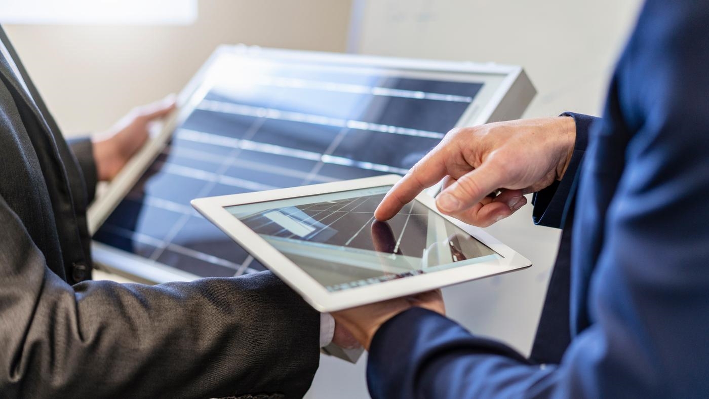 Two businessmen looking at a tablet with a solar panel on it and a solar panel.