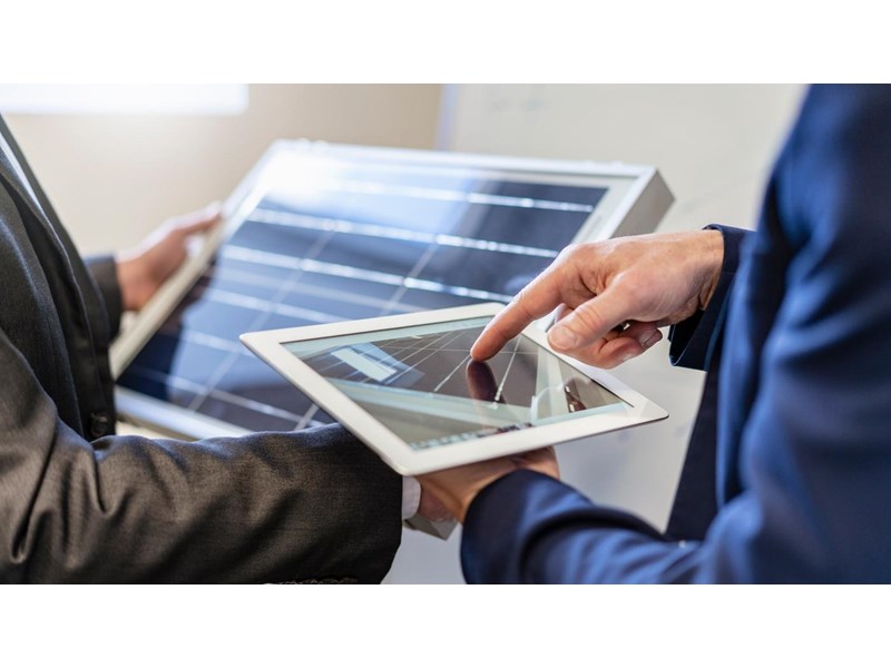Two businessmen looking at a tablet with a solar panel on it and a solar panel.