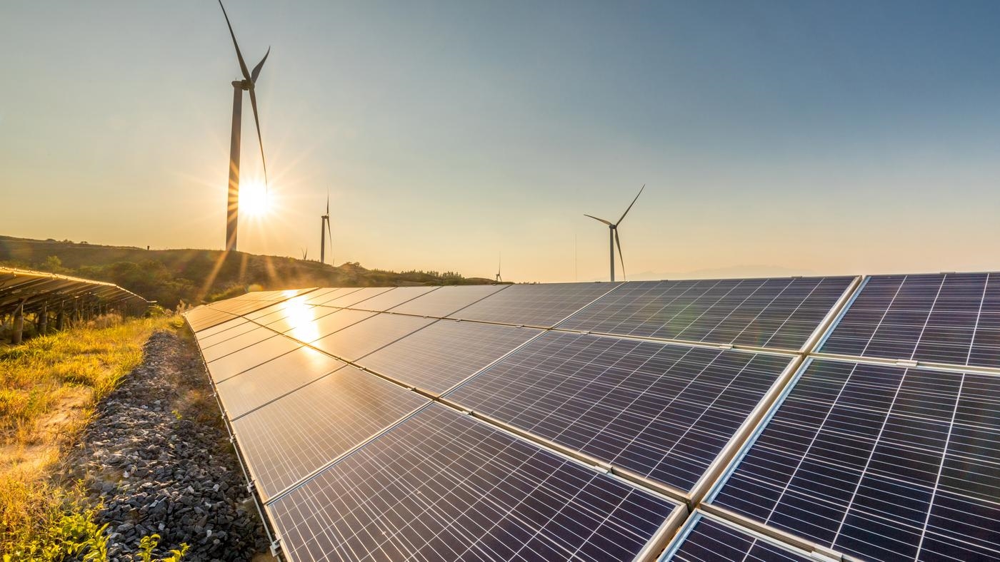 Solar panels and wind turbines in the countryside at sunset.
