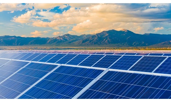 Rows of solar panels in a field, with mountains and blue skies in the background.
