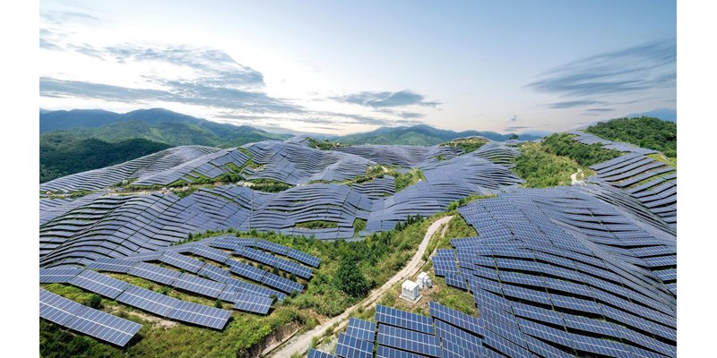 An aerial view of a solar farm, covering many leafy hills.