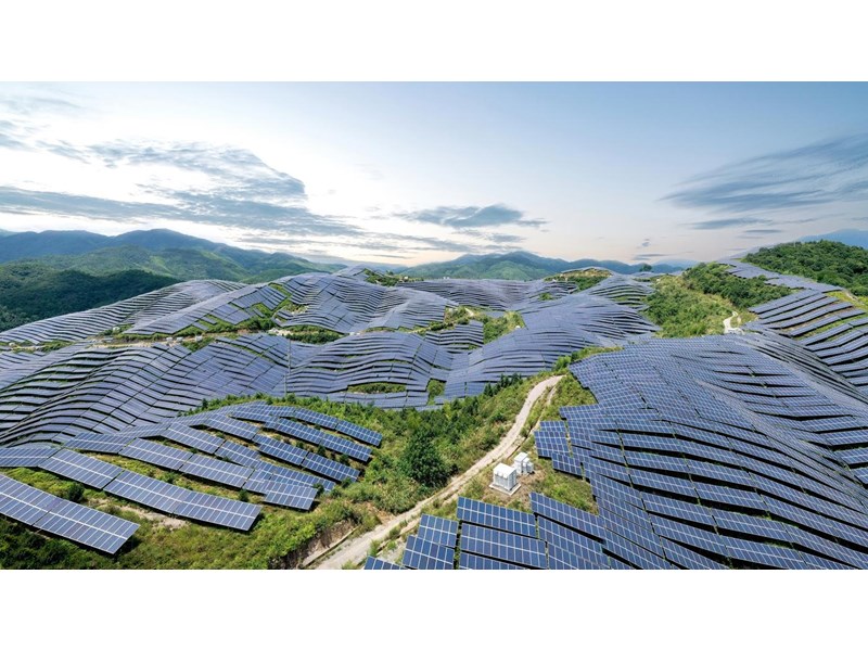 An aerial view of a solar farm, covering many leafy hills.