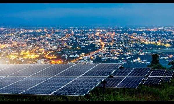 Solar panels on top of a hill overlooking an illuminated city at night.