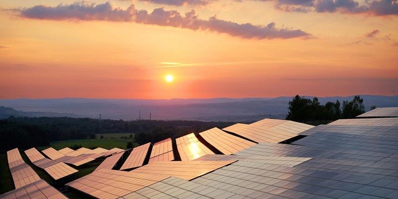 Rows of solar panels on hilltops during sunset.