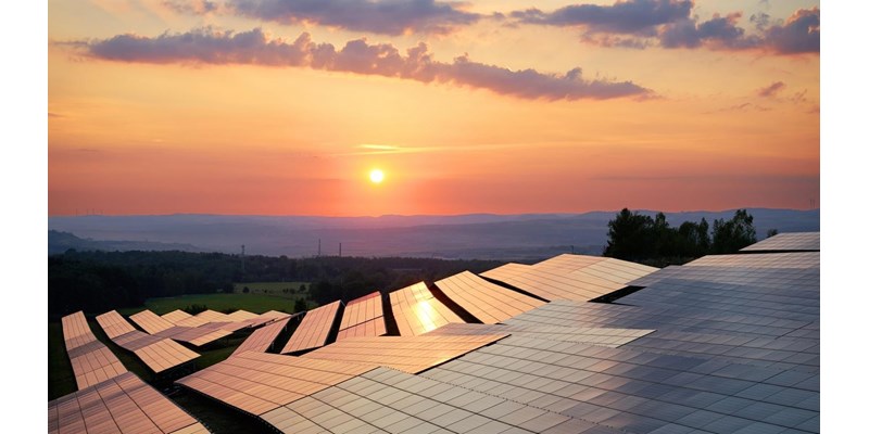 Rows of solar panels on hilltops during sunset.