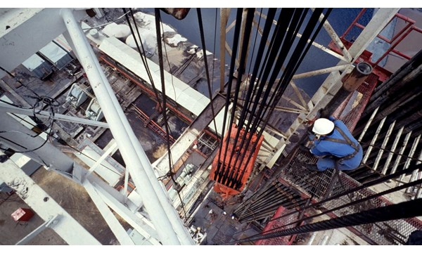 An aerial view of a central column of a drilling rig, with a worker checking the hoist.