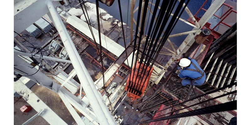 An aerial view of a central column of a drilling rig, with a worker checking the hoist.