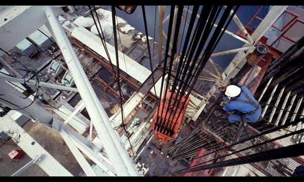 An aerial view of a central column of a drilling rig, with a worker checking the hoist.