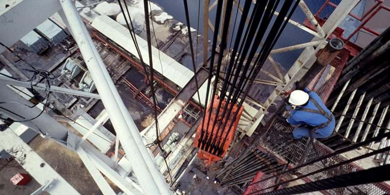 An aerial view of a central column of a drilling rig, with a worker checking the hoist.