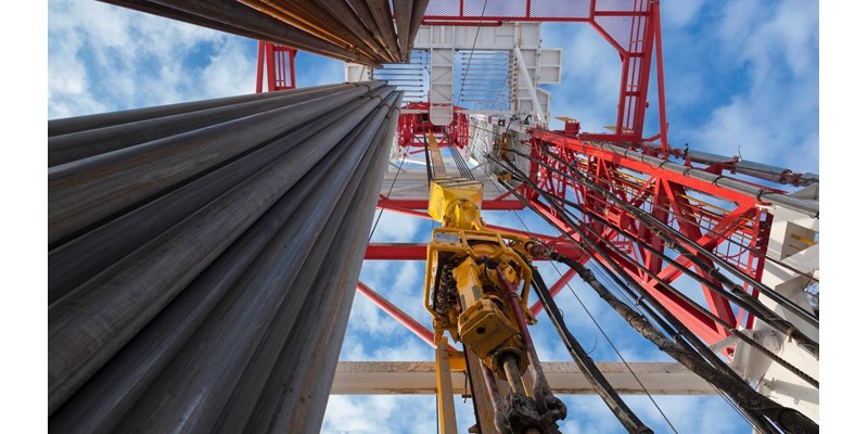 Upward view of a drilling rig with a large pipe and a blue sky.