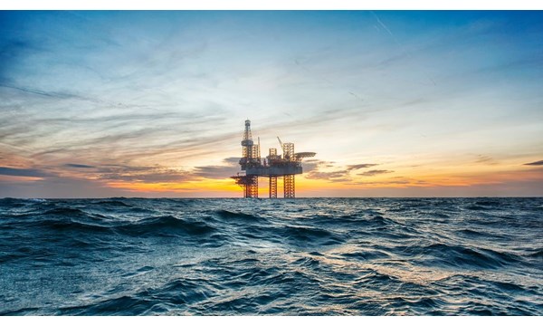 A close-up of an oil rig in the middle of open choppy waters, during an orange sunset.