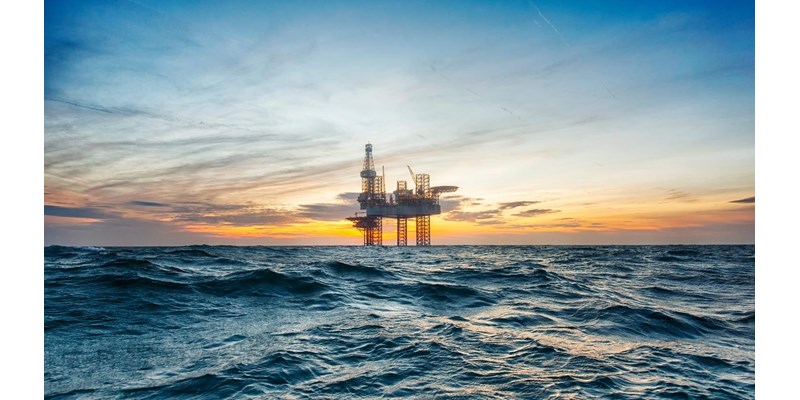 A close-up of an oil rig in the middle of open choppy waters, during an orange sunset.