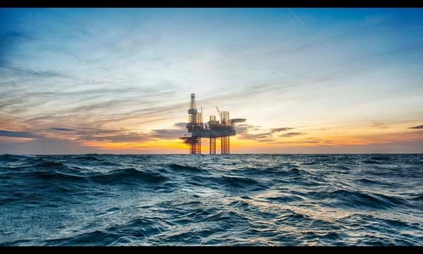 A close-up of an oil rig in the middle of open choppy waters, during an orange sunset.