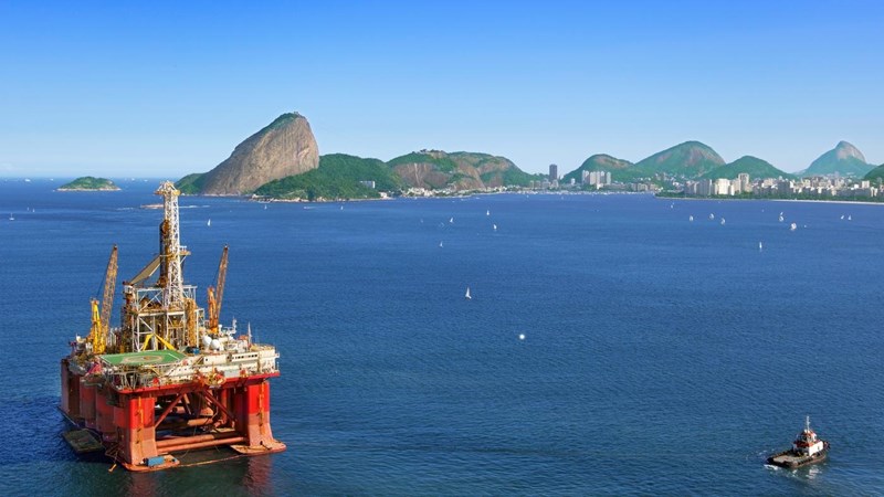 An oil drilling platform and boats, next to a rocky coast.