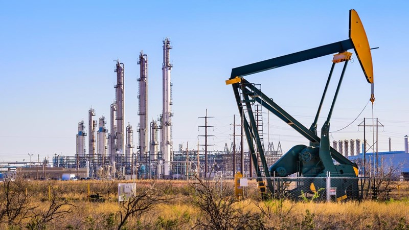 An oil pump in front of an oil refinery, with a network of electricity pylons.