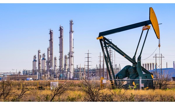 An oil pump in front of an oil refinery, with a network of electricity pylons.