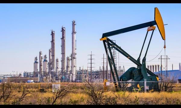 An oil pump in front of an oil refinery, with a network of electricity pylons.