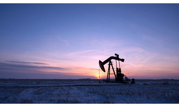 An oil pump in a vast snow covered field at sunset.