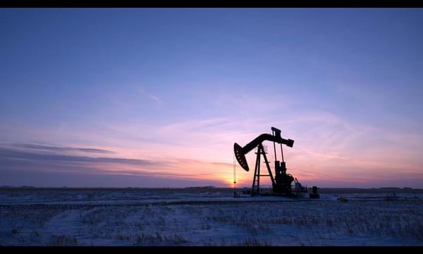 An oil pump in a vast snow covered field at sunset.