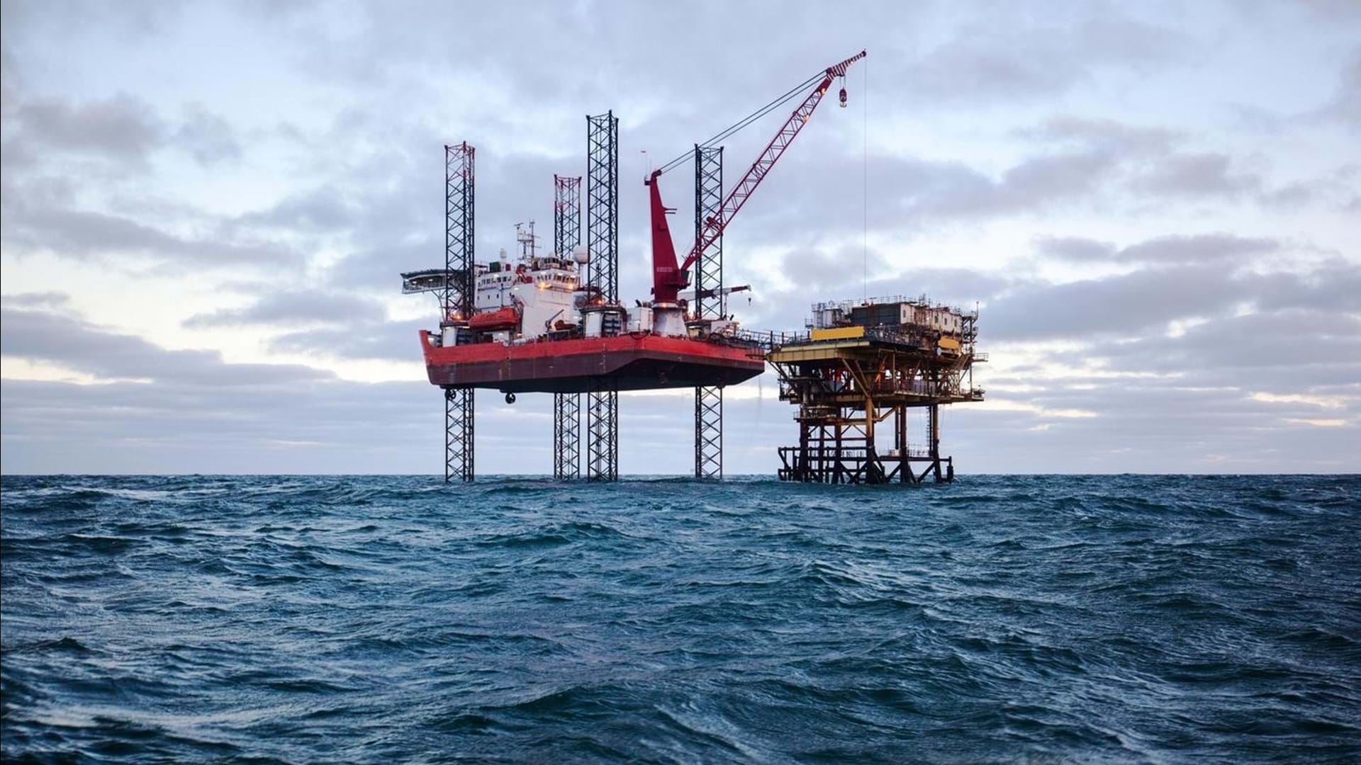 Two oil drilling rigs in open choppy waters.