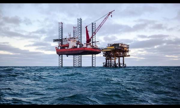 Two oil drilling rigs in open choppy waters.