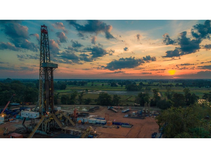 An aerial view of a drilling rig, in country fields at sunset.