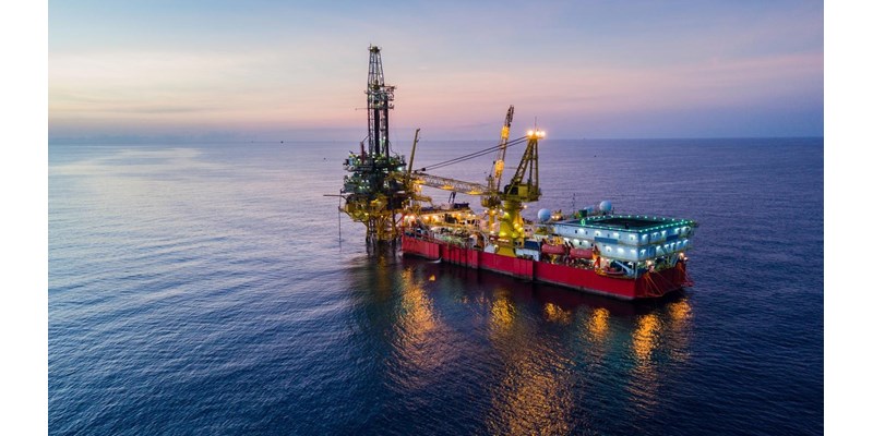 An illuminated oil drilling rig at sea during dusk.