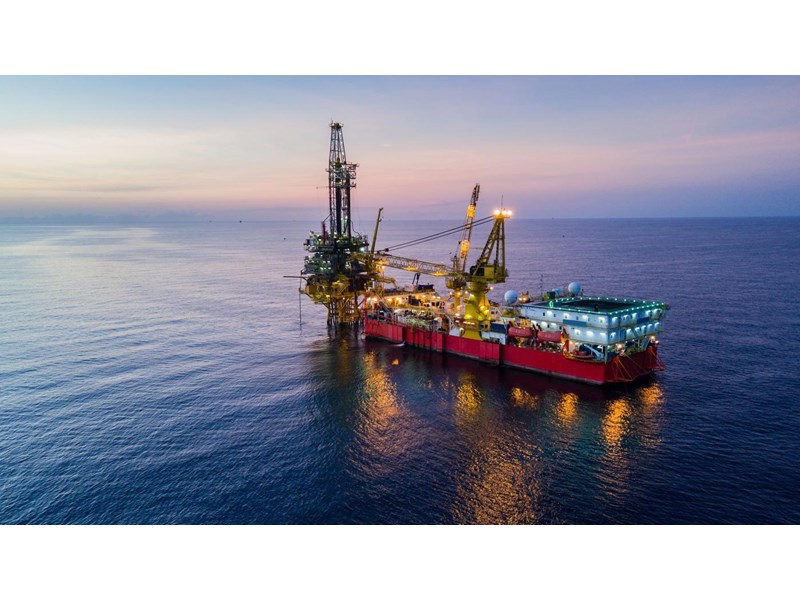 An illuminated oil drilling rig at sea during dusk.