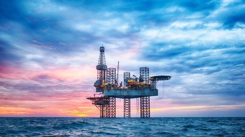 A close-up of an oil rig in open choppy waters, during sunset.