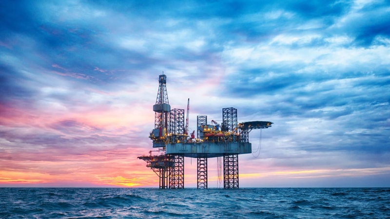 A close-up of an oil rig in open choppy waters, during sunset.